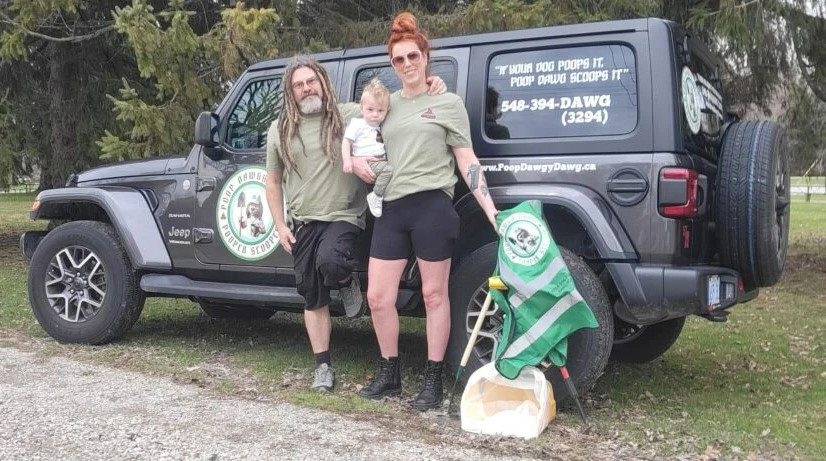 poop-scoop-team Family of three stands beside a dark Jeep with a dog-poop cleanup service logo on the door.